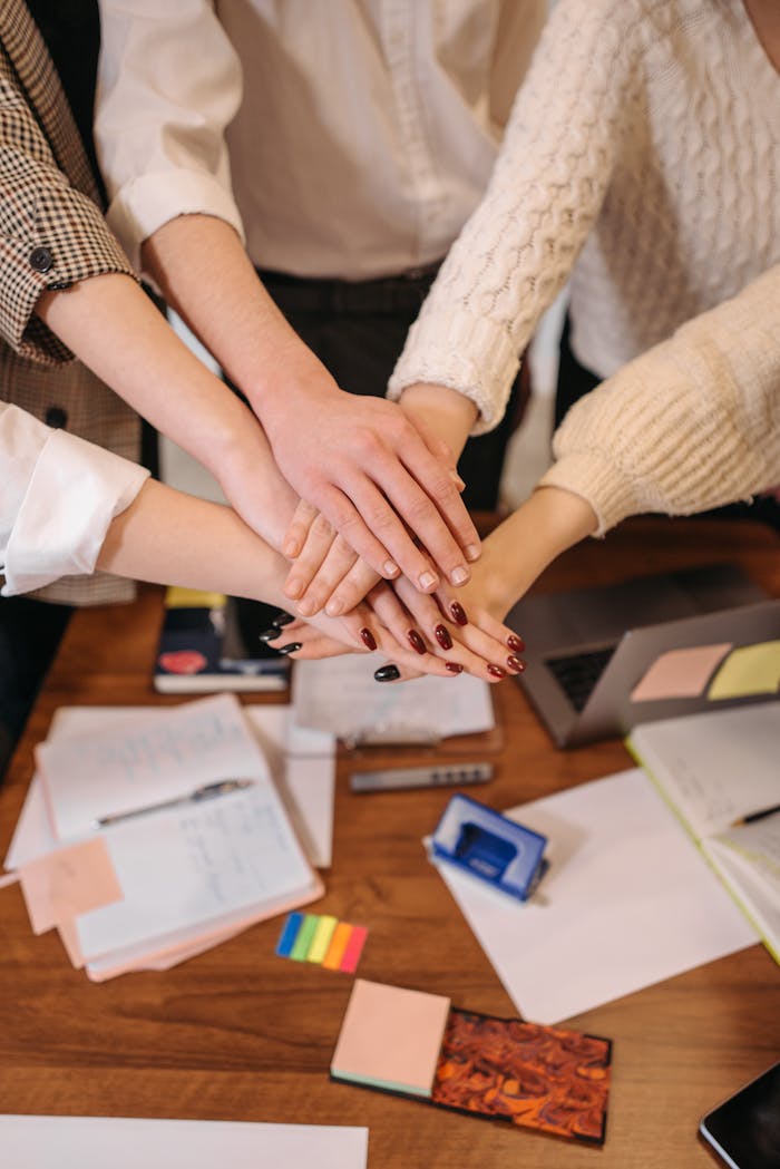 journey A top-down view of hands stacked together over an office table, symbolizing teamwork.